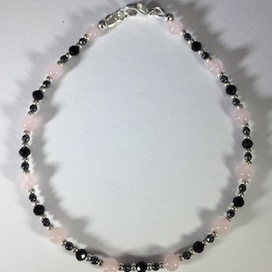 May include: A delicate bracelet made with alternating pink and black beads. The bracelet is made with small, round beads and has a silver clasp.
