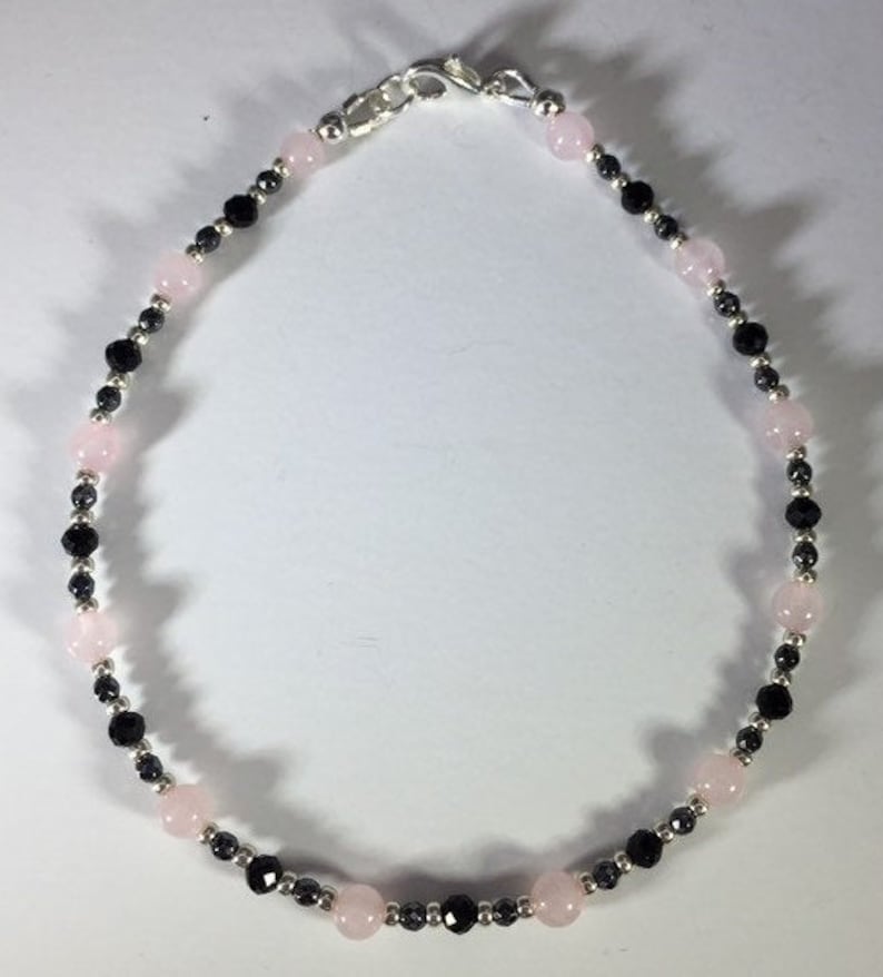 May include: A delicate bracelet made with alternating pink and black beads. The bracelet is made with small, round beads and has a silver clasp.