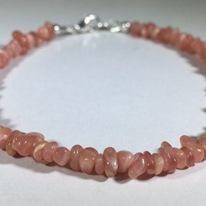 May include: A delicate bracelet featuring small, irregular pink gemstones strung together. The bracelet is secured with a silver-colored clasp. The gemstones have a natural, slightly translucent appearance, and the bracelet is displayed on a white surface.