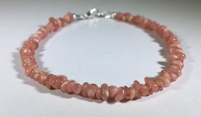 May include: A delicate bracelet featuring small, irregular pink gemstones strung together. The bracelet is secured with a silver-colored clasp. The gemstones have a natural, slightly translucent appearance, and the bracelet is displayed on a white surface.