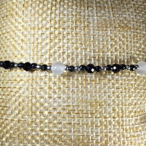 May include: A black and white beaded bracelet with silver accents. The bracelet features alternating black and white beads, with two larger white beads.