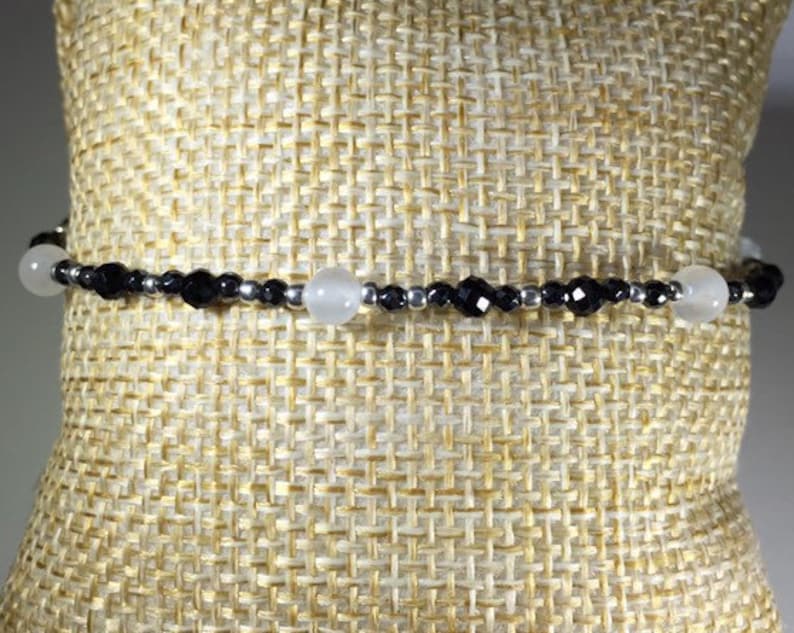 May include: A black and white beaded bracelet with silver accents. The bracelet features alternating black and white beads, with two larger white beads.
