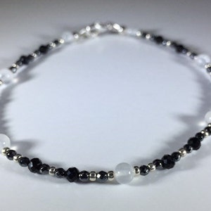 May include: A black and white beaded bracelet with silver accents. The bracelet features alternating black and white beads, with larger white beads spaced throughout.