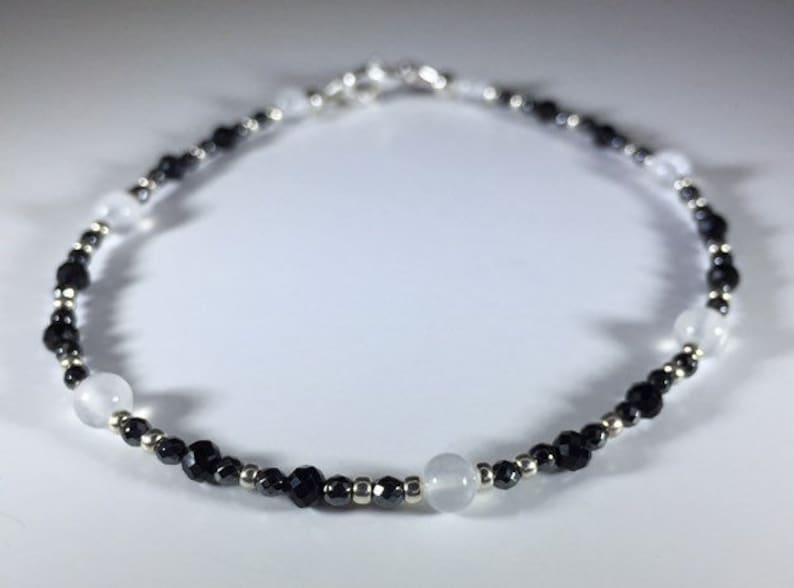 May include: A black and white beaded bracelet with silver accents. The bracelet features alternating black and white beads, with larger white beads spaced throughout.