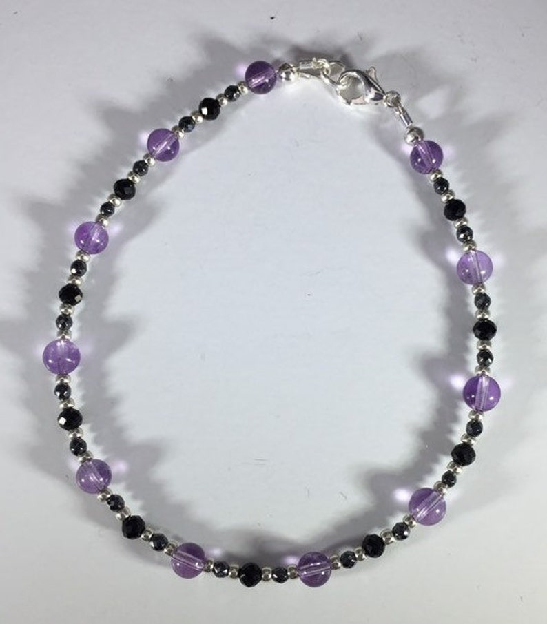 May include: A silver chain bracelet with alternating amethyst and black beads.