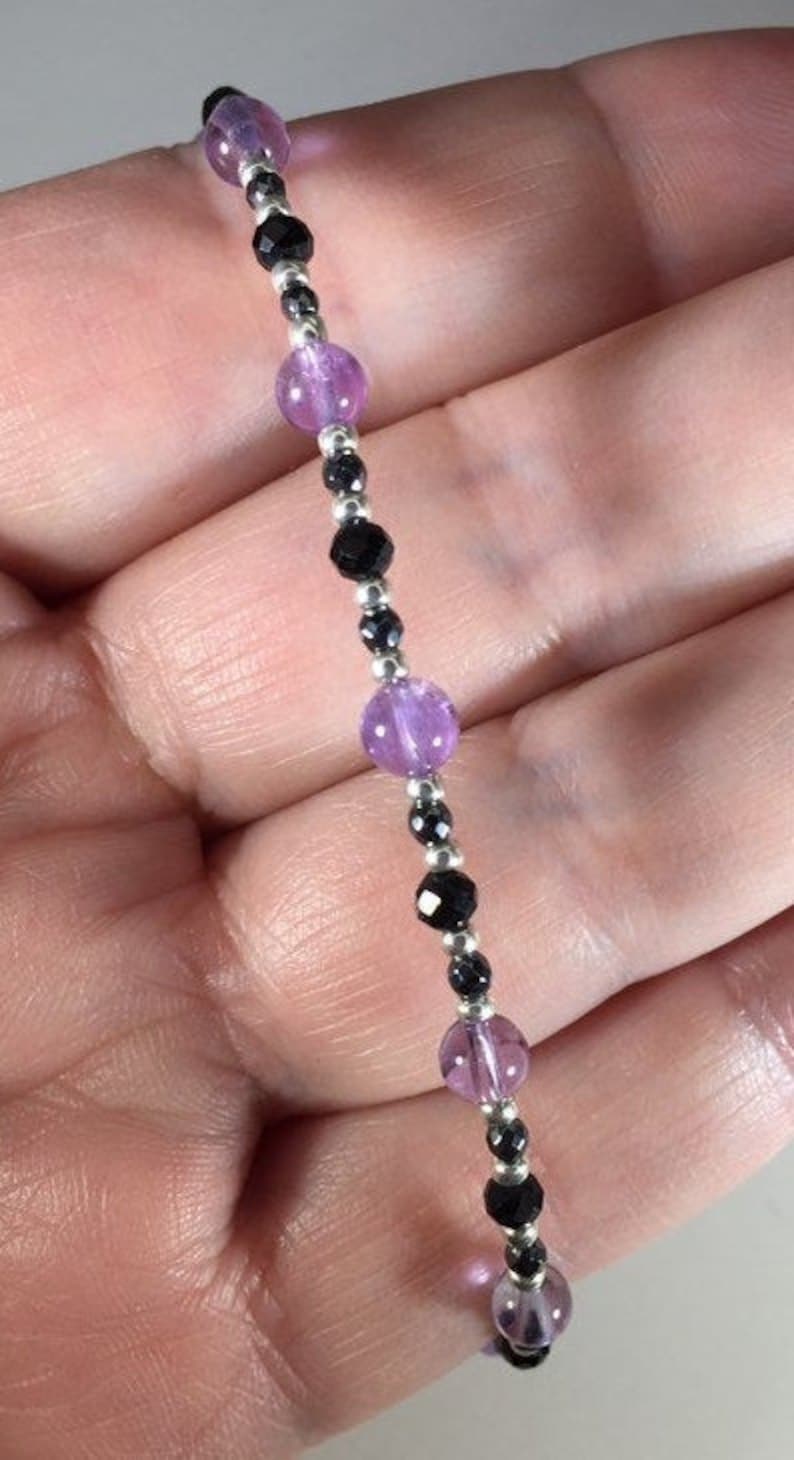 May include: A bracelet featuring alternating amethyst and black onyx beads. The bracelet is made with silver beads and is strung on elastic.