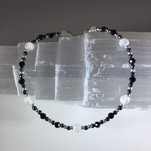 May include: A black and white beaded bracelet with alternating black and white beads. The bracelet is made with black onyx and white moonstone beads.