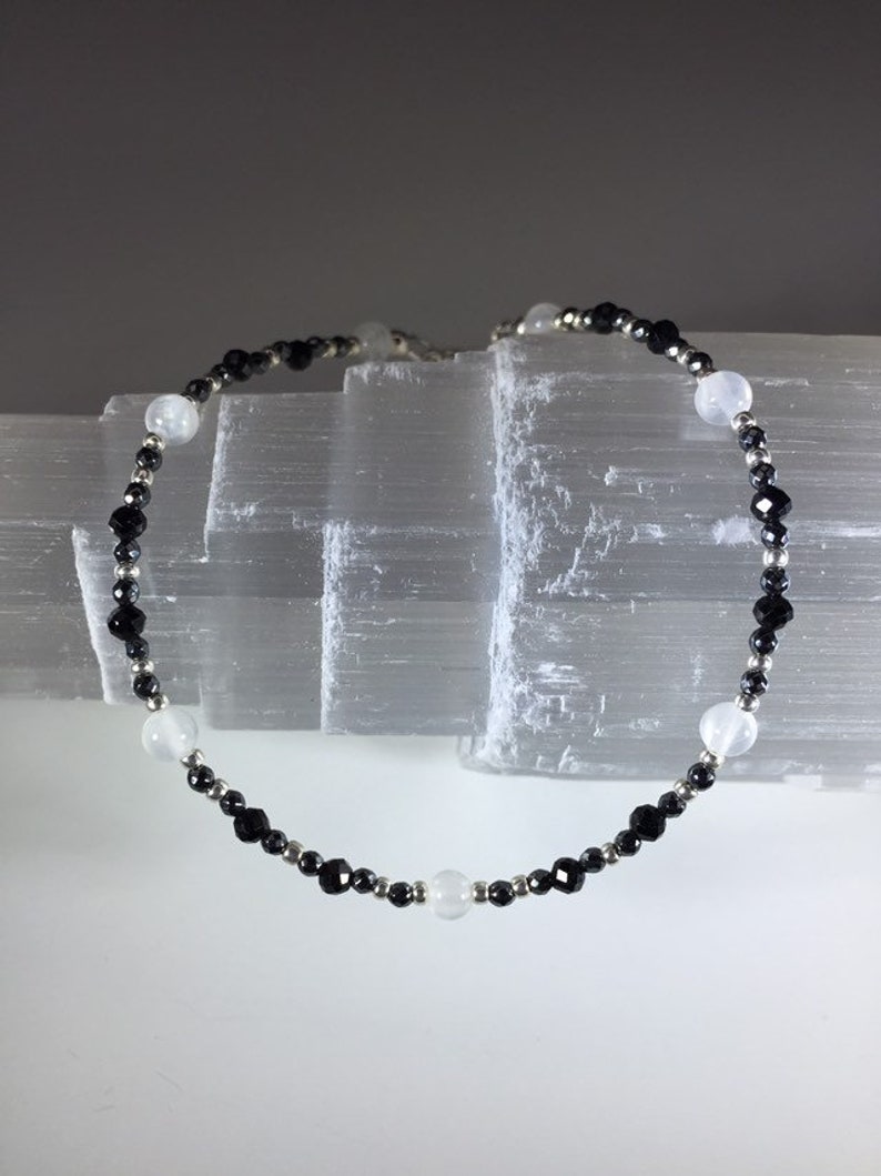 May include: A black and white beaded bracelet with alternating black and white beads. The bracelet is made with black onyx and white moonstone beads.