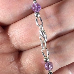 May include: A silver chain bracelet with alternating amethyst and black beads.