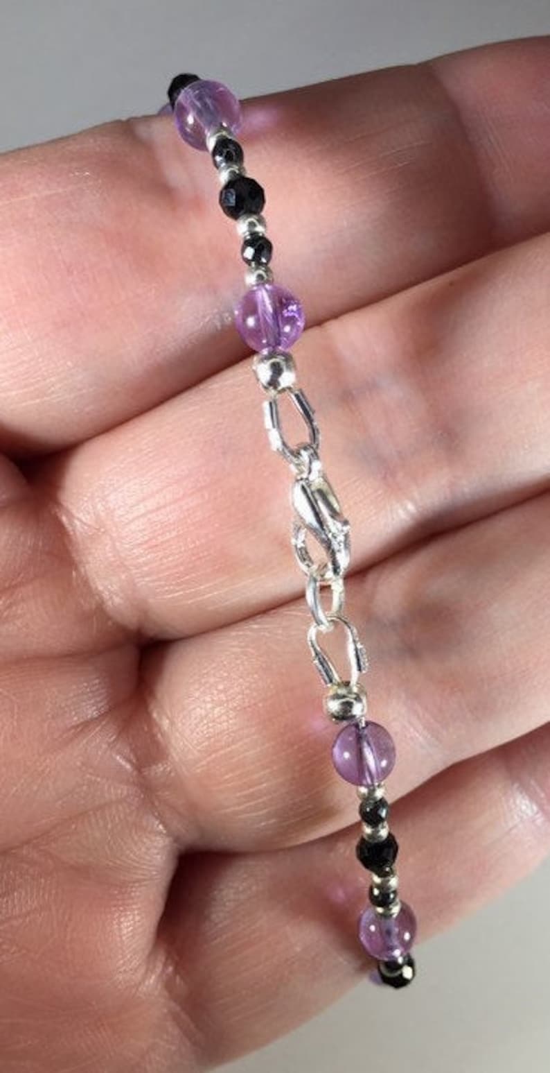 May include: A silver chain bracelet with alternating amethyst and black beads.