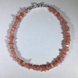 May include: A delicate bracelet featuring small, irregularly shaped, peach-colored gemstones. The stones are strung together, creating a continuous loop. The bracelet is secured with a silver-colored clasp.