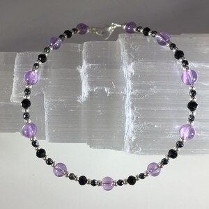 May include: A delicate anklet with alternating black and silver beads and amethyst gemstones.