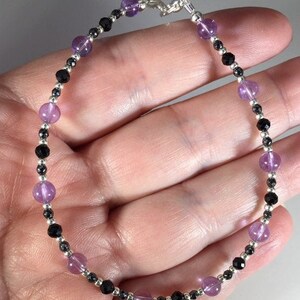 May include: A silver chain bracelet with alternating amethyst and black beads.