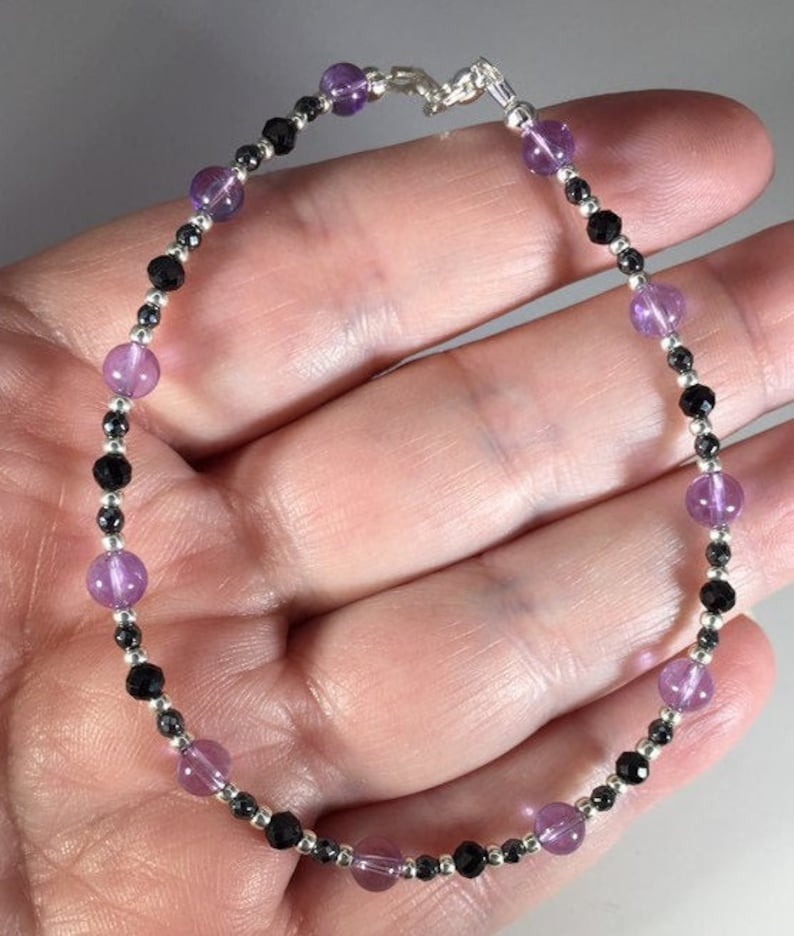May include: A silver chain bracelet with alternating amethyst and black beads.