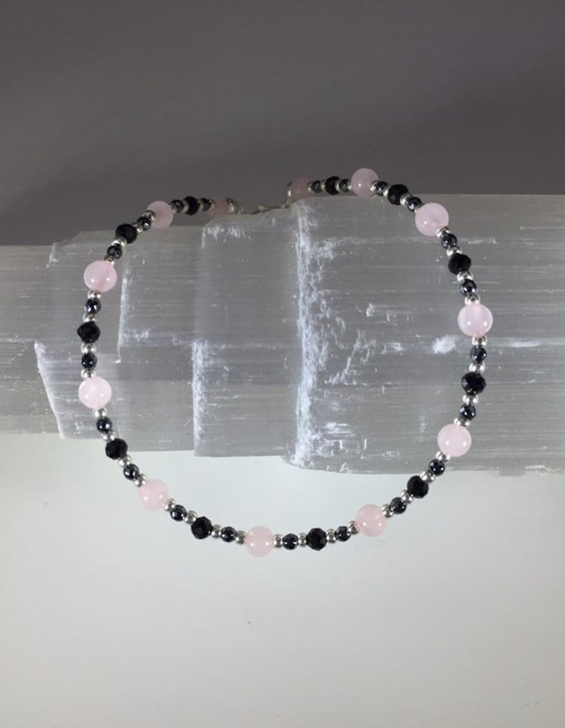 May include: A bracelet made with alternating black and pink beads. The bracelet is made with small silver beads between each larger bead.