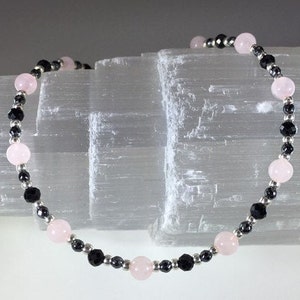 May include: A bracelet made with black and pink beads. The bracelet is made with small black beads and larger pink beads.