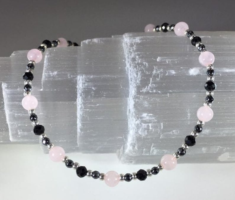 May include: A bracelet made with black and pink beads. The bracelet is made with small black beads and larger pink beads.