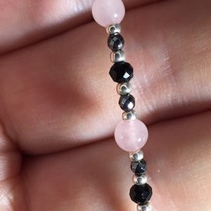 May include: A bracelet made with alternating pink and black beads. The bracelet is made with small, round pink beads and faceted black beads.