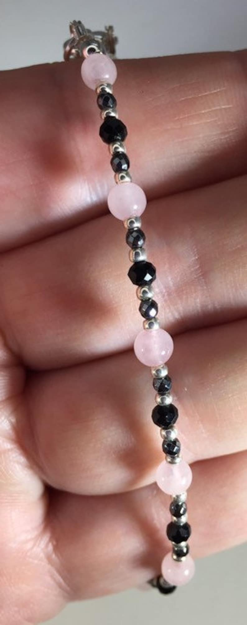 May include: A bracelet made with alternating pink and black beads. The bracelet is made with small, round pink beads and faceted black beads.