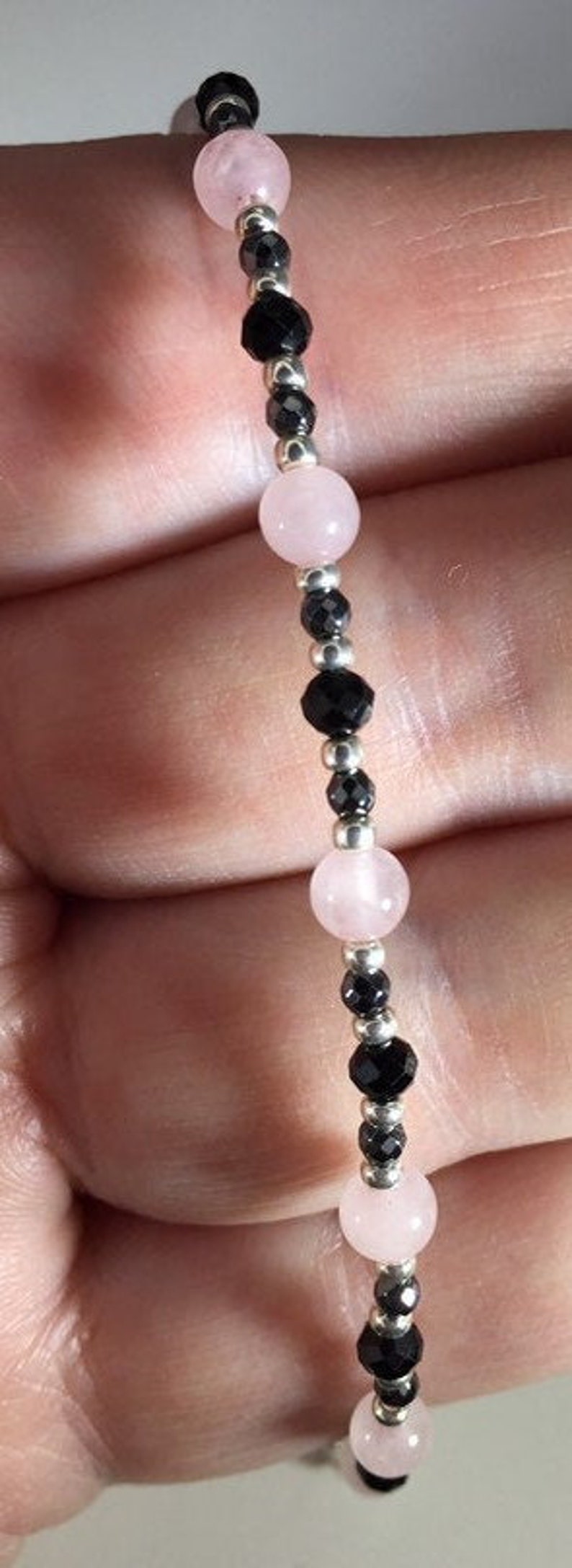 May include: A bracelet made with pink and black beads. The bracelet is made with alternating pink and black beads, with silver beads in between.