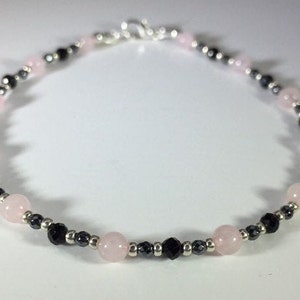 May include: A delicate bracelet made with alternating pink and black beads. The bracelet is made with small, round beads and has a silver clasp.