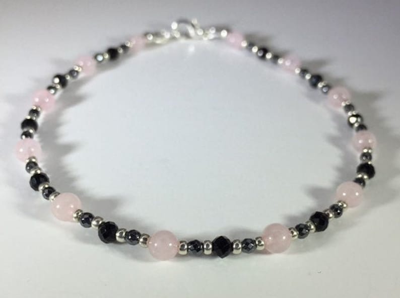 May include: A delicate bracelet made with alternating pink and black beads. The bracelet is made with small, round beads and has a silver clasp.