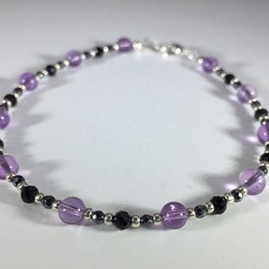 May include: A delicate bracelet featuring alternating amethyst and black beads, with silver spacers.