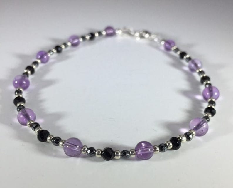 May include: A delicate bracelet featuring alternating amethyst and black beads, with silver spacers.