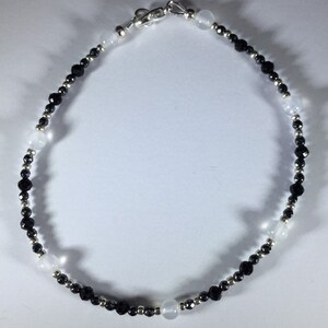May include: A black and white beaded anklet with a silver clasp. The anklet is made with small black beads and larger white beads.