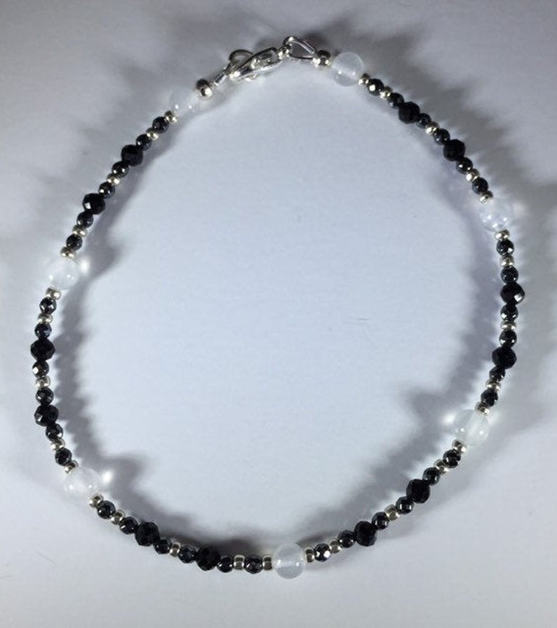 May include: A black and white beaded anklet with a silver clasp. The anklet is made with small black beads and larger white beads.
