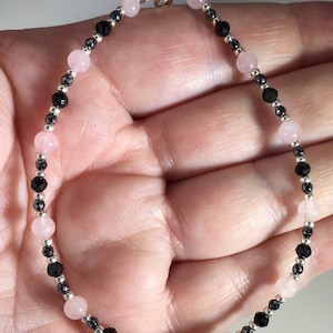 May include: A delicate bracelet with alternating pink and black beads. The bracelet is made with rose quartz and black onyx beads, and has a silver clasp.
