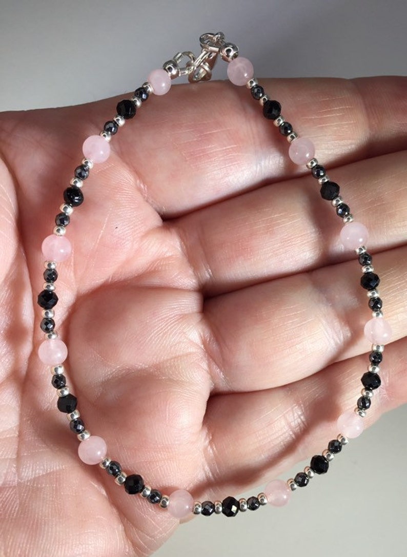 May include: A delicate bracelet with alternating pink and black beads. The bracelet is made with rose quartz and black onyx beads, and has a silver clasp.