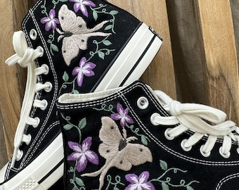 May include: Black high-top canvas sneakers with white laces and embroidered floral designs featuring butterflies. The butterflies are beige with brown accents and the flowers are purple.