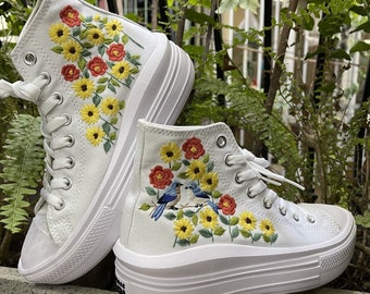 May include: White high-top platform sneakers with embroidered floral designs and blue birds. The flowers are yellow, red, and white.