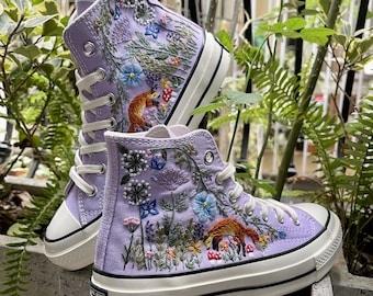 May include: A pair of lavender high-top sneakers with embroidered floral designs and foxes. The sneakers have white soles and laces.