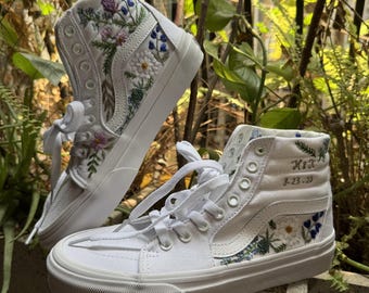 May include: White high-top canvas sneakers with floral embroidery and the text "H.I.X 8.23.29" on one shoe.