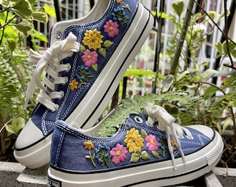 May include: A pair of blue canvas sneakers with white soles and laces. The sneakers are decorated with embroidered flowers in shades of pink, yellow, and green.