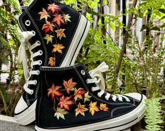 May include: A pair of black high-top canvas sneakers with white soles and orange and yellow embroidered maple leaves.