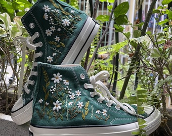 May include: Green high-top canvas sneakers with white embroidered flowers and green leaves. The shoes have white laces and a white rubber sole.