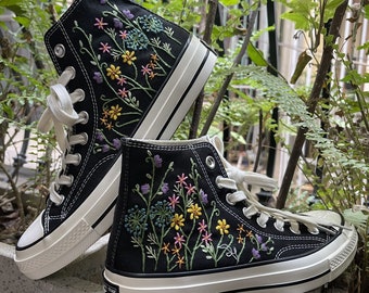 May include: A pair of black high-top canvas sneakers with white soles and laces. The sneakers are embroidered with colorful flowers and greenery.