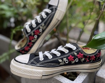 May include: A pair of black canvas sneakers with white laces and red floral embroidery. The sneakers have a white rubber sole.