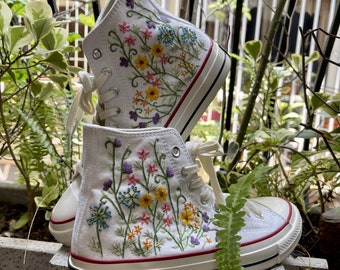 May include: White high-top sneakers with colorful floral embroidery. The embroidery features a variety of flowers and leaves in shades of pink, yellow, blue, and purple.