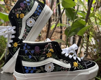 May include: Black high-top canvas sneakers with white stitching and a white stripe. The sneakers are embroidered with colorful flowers and leaves.