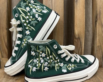 May include: A pair of green high-top canvas sneakers with white embroidered flowers and leaves. The sneakers have white laces and a white rubber sole.