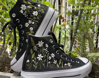 May include: Black high-top sneakers with white embroidered flowers and green leaves. The sneakers have a thick white sole.