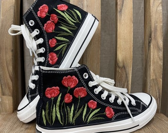May include: A pair of black high-top canvas sneakers with red poppy flower embroidery. The sneakers have white laces and a white rubber sole.