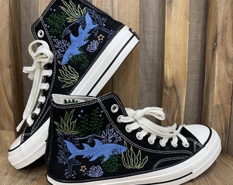 May include: Black high-top canvas sneakers with white soles and blue embroidered sharks and coral reef designs.