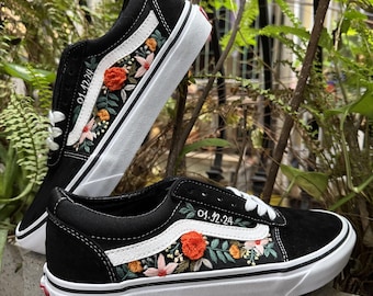 May include: Black canvas sneakers with white stitching and a white stripe. The shoes have embroidered flowers and leaves in shades of red, orange, yellow, and green. The text "01.12.24" is embroidered on the side of the shoe.