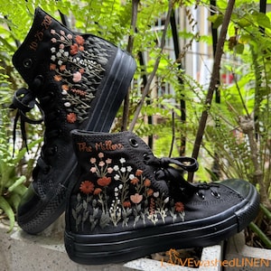 May include: A pair of black high-top canvas shoes with embroidered floral designs and the text "The Millers" and "10-23-202".