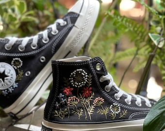 May include: Black high-top canvas sneakers with white soles and embroidered floral designs in red, green, and white.